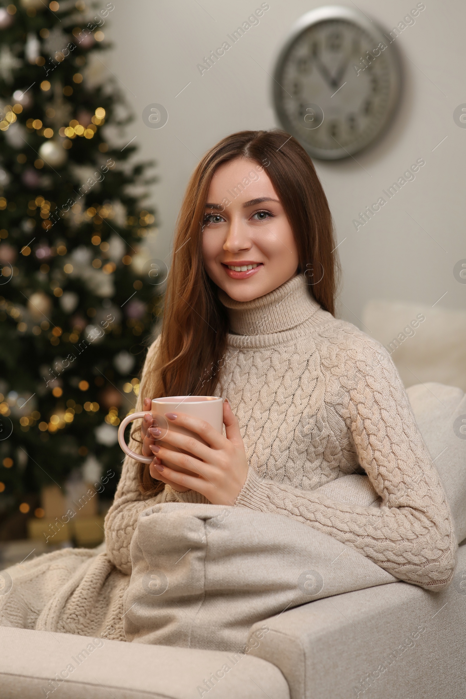 Photo of Beautiful young smiling woman with cup of tea near Christmas tree at home