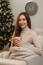 Photo of Beautiful young smiling woman with cup of tea near Christmas tree at home