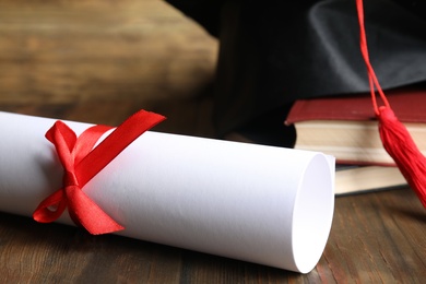 Photo of Graduation hat, books and student's diploma on wooden table, closeup