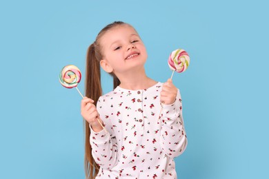 Photo of Happy little girl with colorful lollipops on light blue background