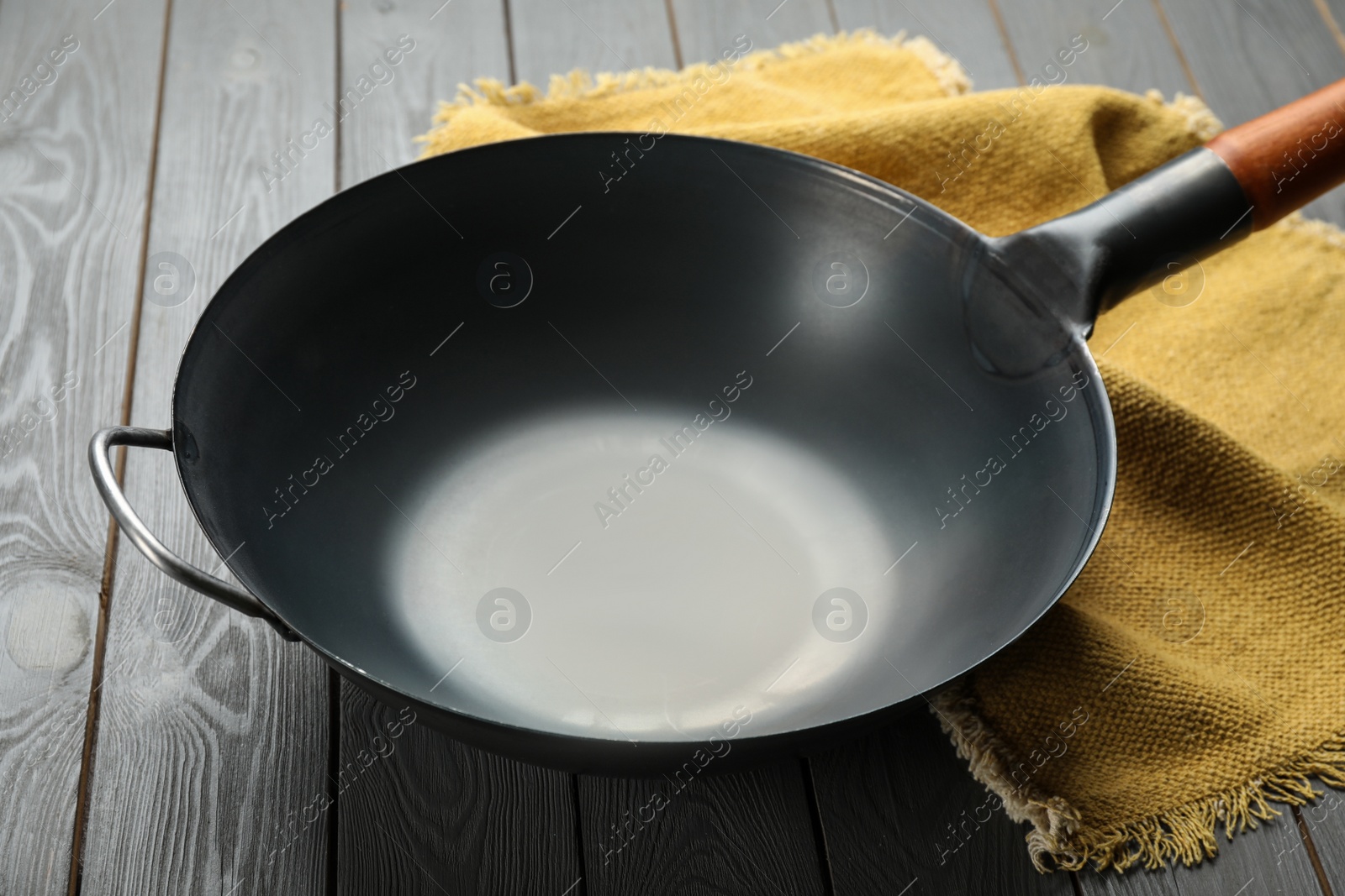 Photo of Empty iron wok and napkin on grey wooden table