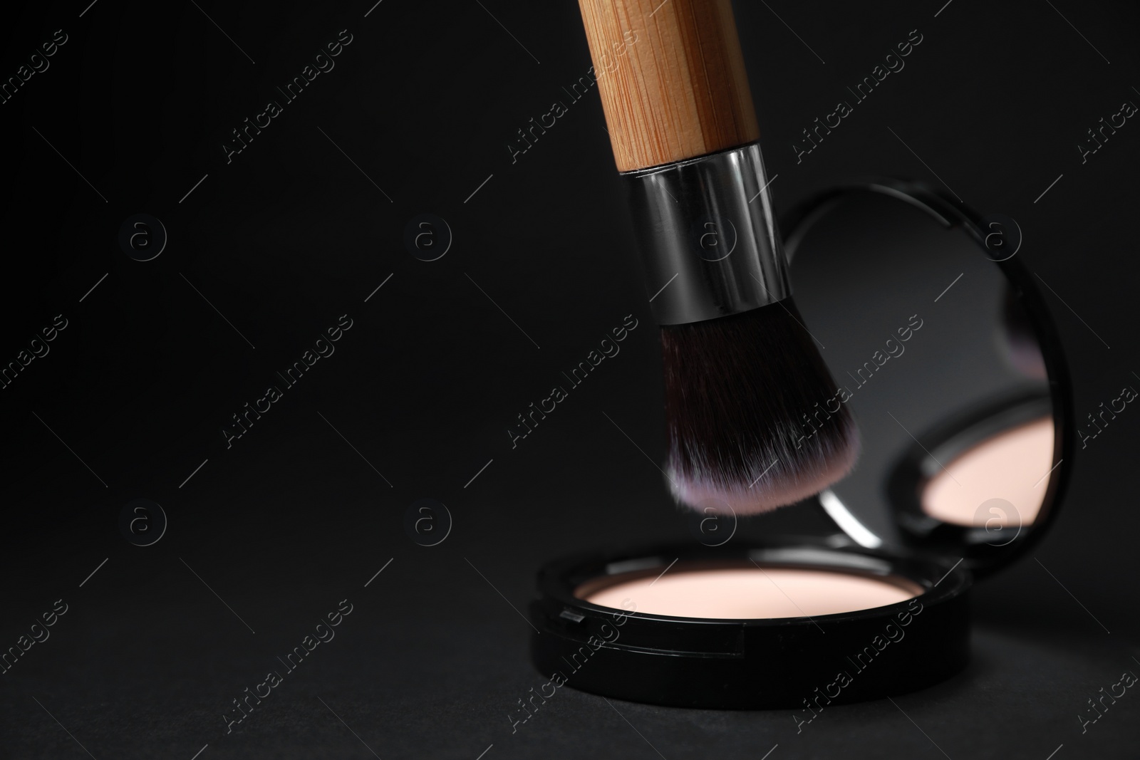 Photo of Makeup brush over face powder on black background, space for text