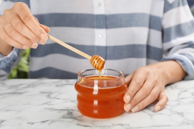 Photo of Woman pouring honey into glass jar at table, closeup