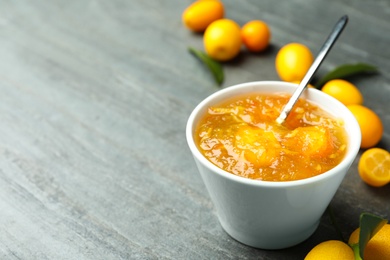 Photo of Delicious kumquat jam in bowl and fresh fruits on grey table, space for text