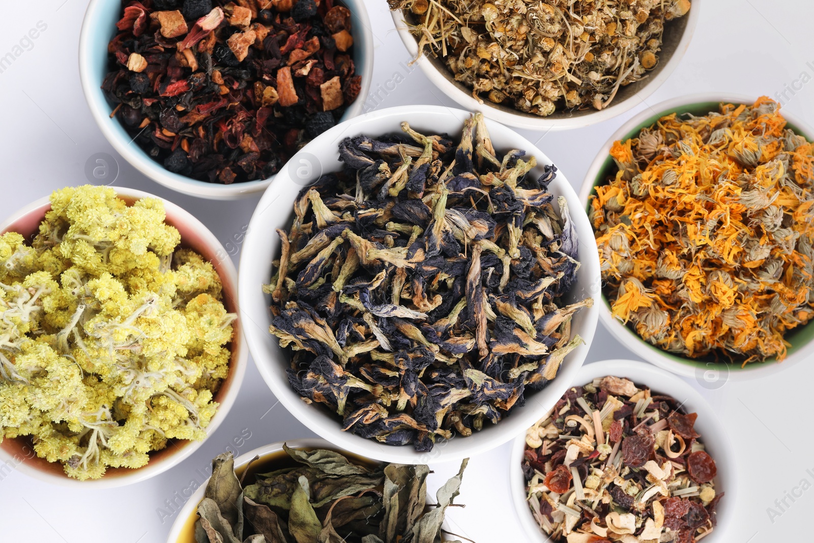 Photo of Many different dry herbs and flowers in bowls on white background, flat lay