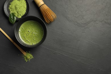 Cup of fresh matcha tea, bamboo whisk, spoon and green powder on black table, flat lay. Space for text