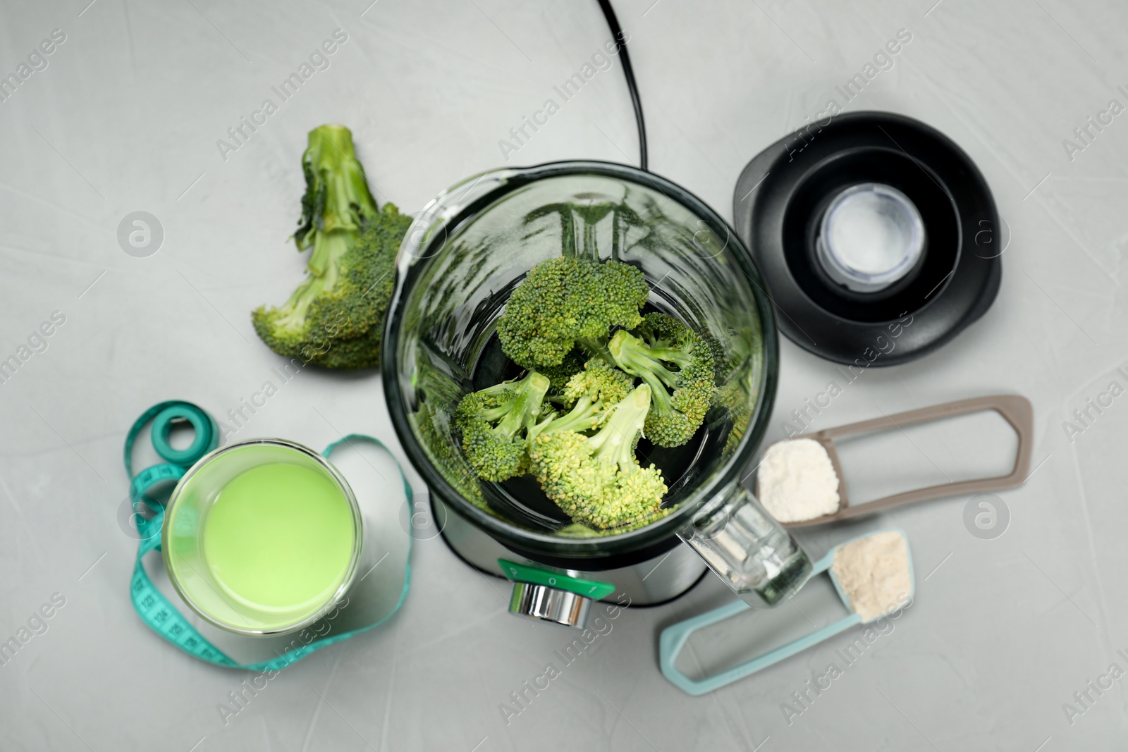 Photo of Making shake. Broccoli in blender and scoops with different powders on light gray table, flat lay