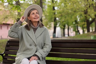 Photo of Beautiful senior woman sitting on bench in park, space for text