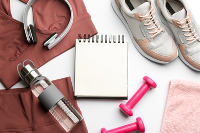 Photo of Flat lay composition with sportswear, notebook and dumbbells on white background. Gym workout plan