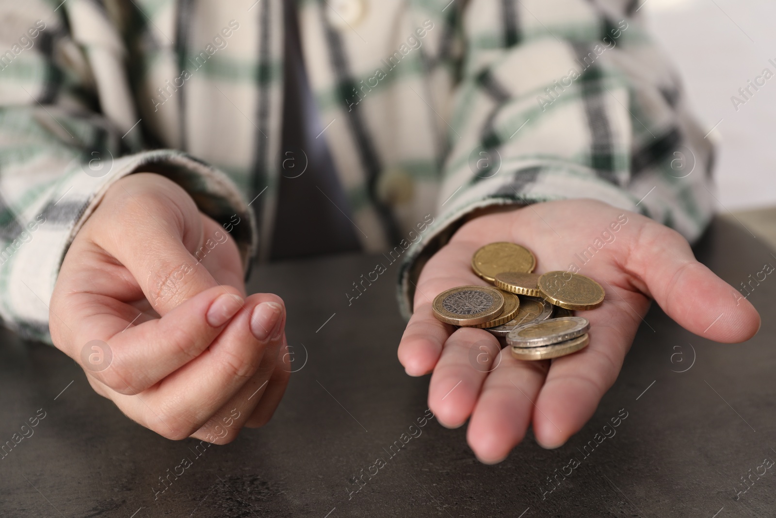 Photo of Poor woman holding coins at grey table indoors, closeup