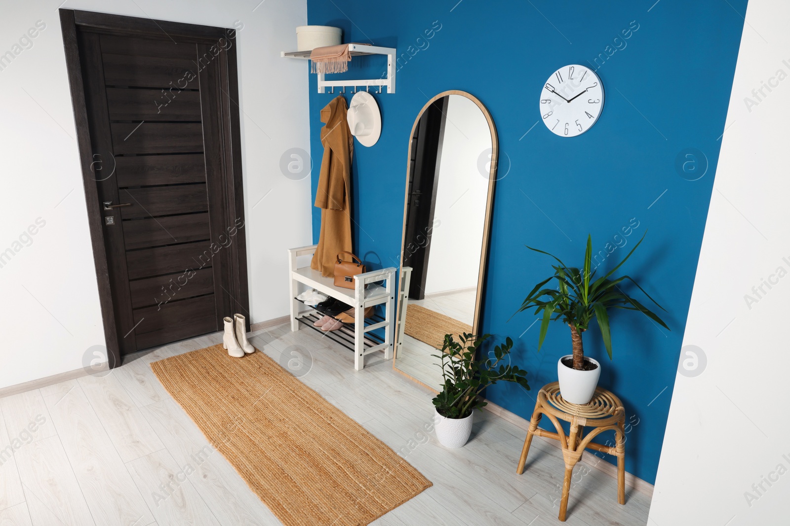 Photo of Stylish hallway with shoe storage bench and mirror near blue wall. Interior design