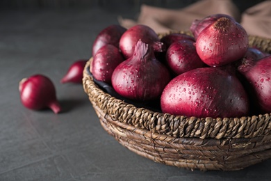 Photo of Wicker bowl of wet whole red onion bulbs on grey table, closeup