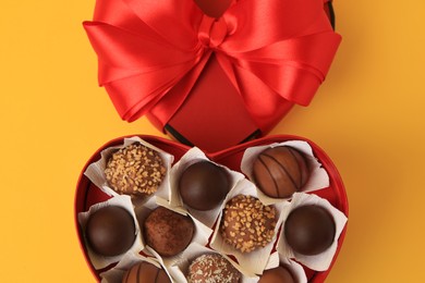 Photo of Heart shaped box with delicious chocolate candies on yellow background, flat lay