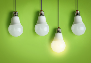 Image of Idea concept. Glowing light bulb among others on green background 