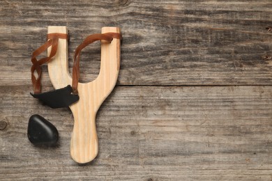 Photo of Slingshot with pebble on wooden background, top view. Space for text