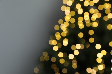 Photo of Blurred view of beautiful fir tree with Christmas lights on grey background, closeup. Space for text