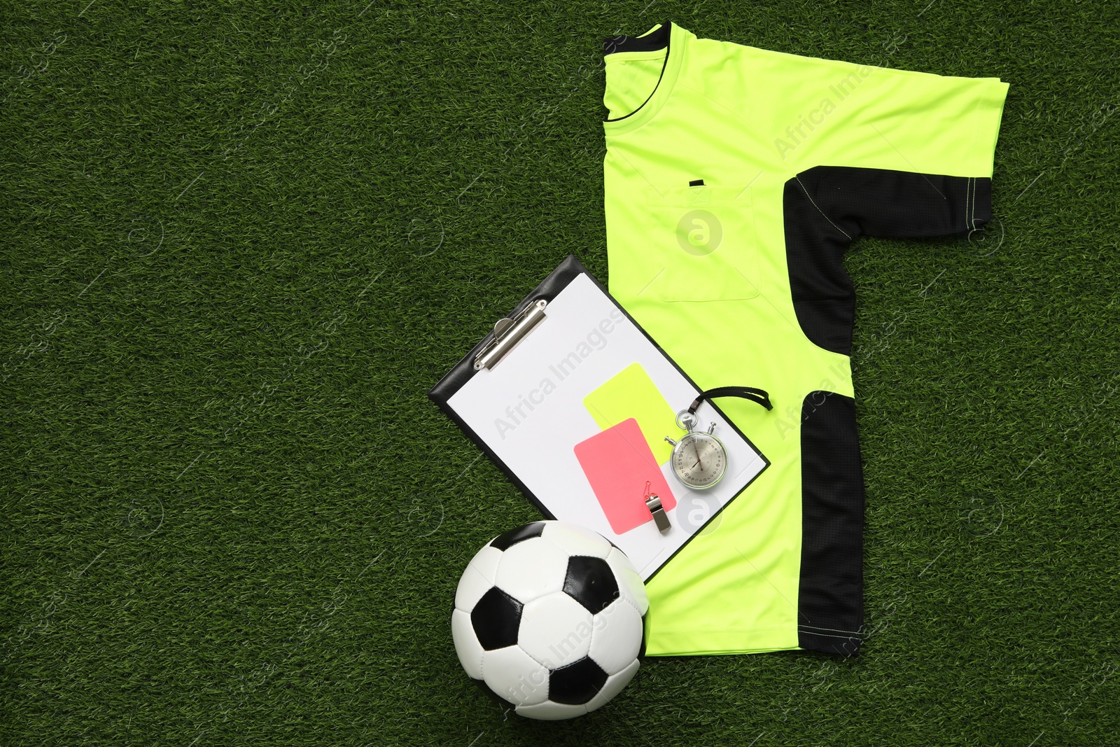 Photo of Uniform, soccer ball and other referee equipment on green grass, top view. Space for text