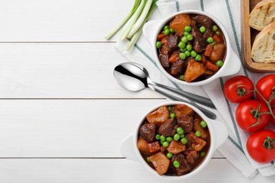 Delicious beef stew with carrots, peas and potatoes served on white wooden table, flat lay. Space for text