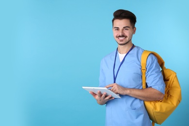 Young medical student with tablet and backpack on color background. Space for text