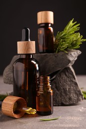 Photo of Essential oil in bottles, dropper and rosemary on grey table