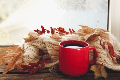 Cup of hot drink and autumn leaves near window on rainy day. Cozy atmosphere