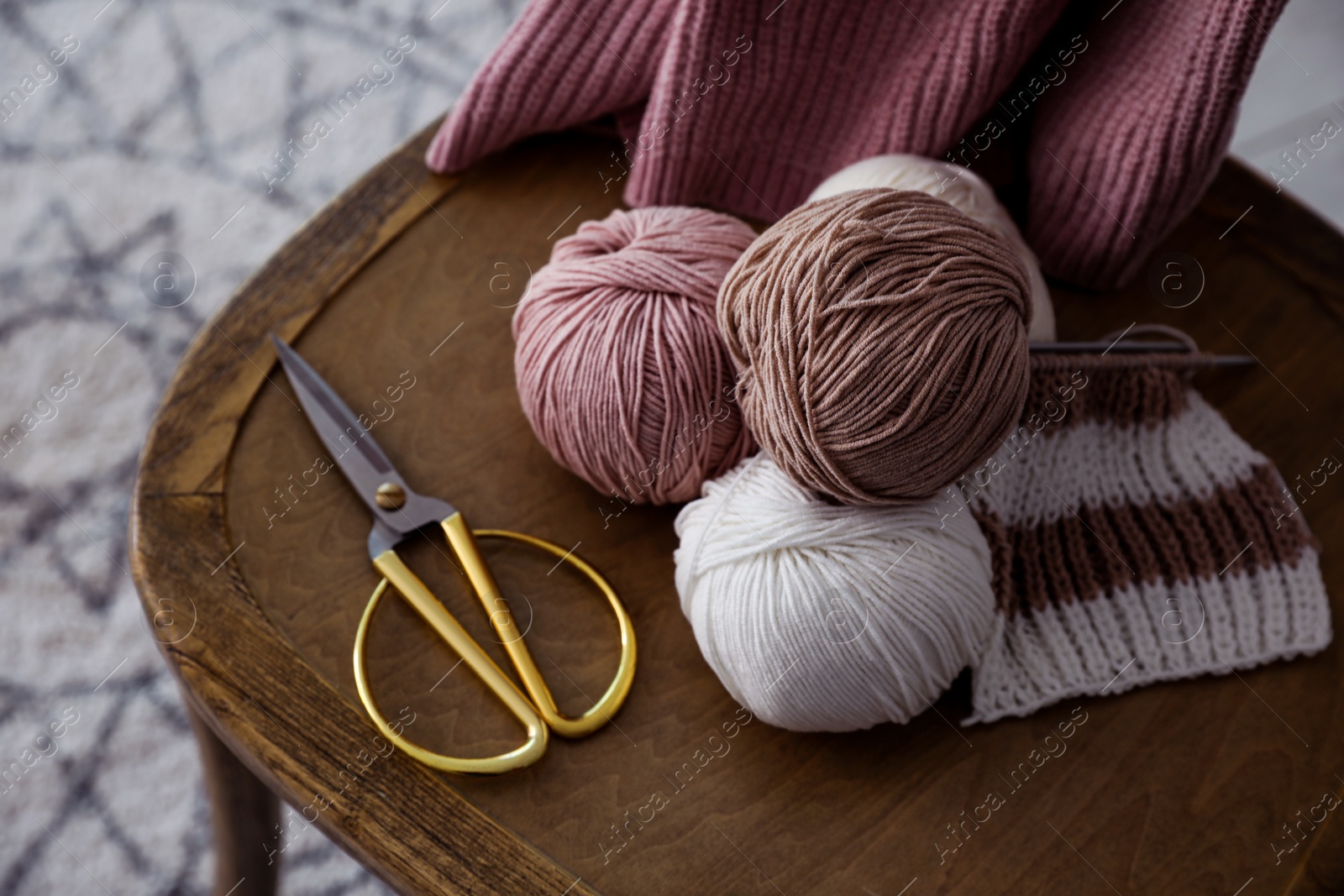 Photo of Yarn balls and scissors on wooden chair indoors, closeup. Creative hobby