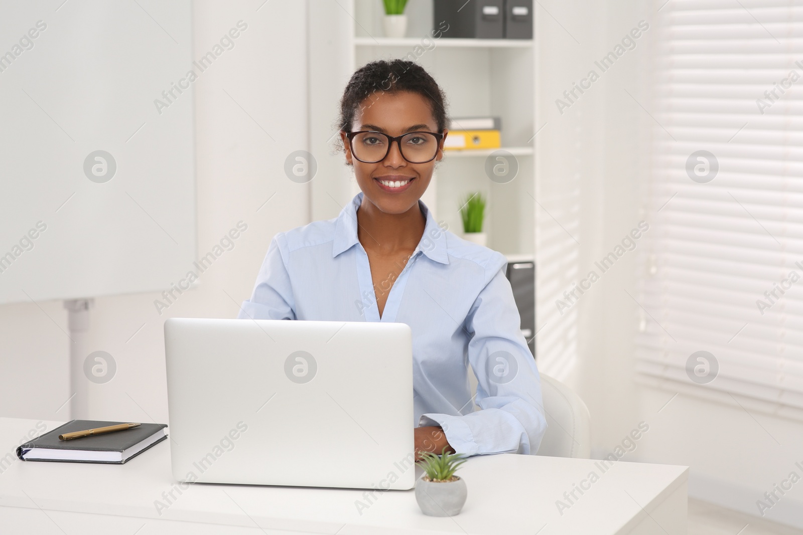 Photo of Smiling African American intern working on laptop at white table in office