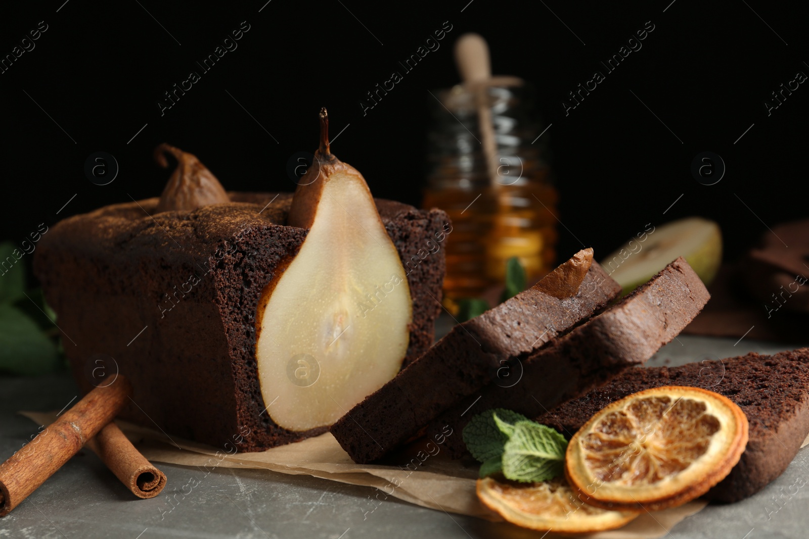 Photo of Tasty pear bread with cinnamon, mint and dried orange slices on grey table. Homemade cake