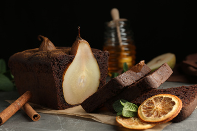 Photo of Tasty pear bread with cinnamon, mint and dried orange slices on grey table. Homemade cake