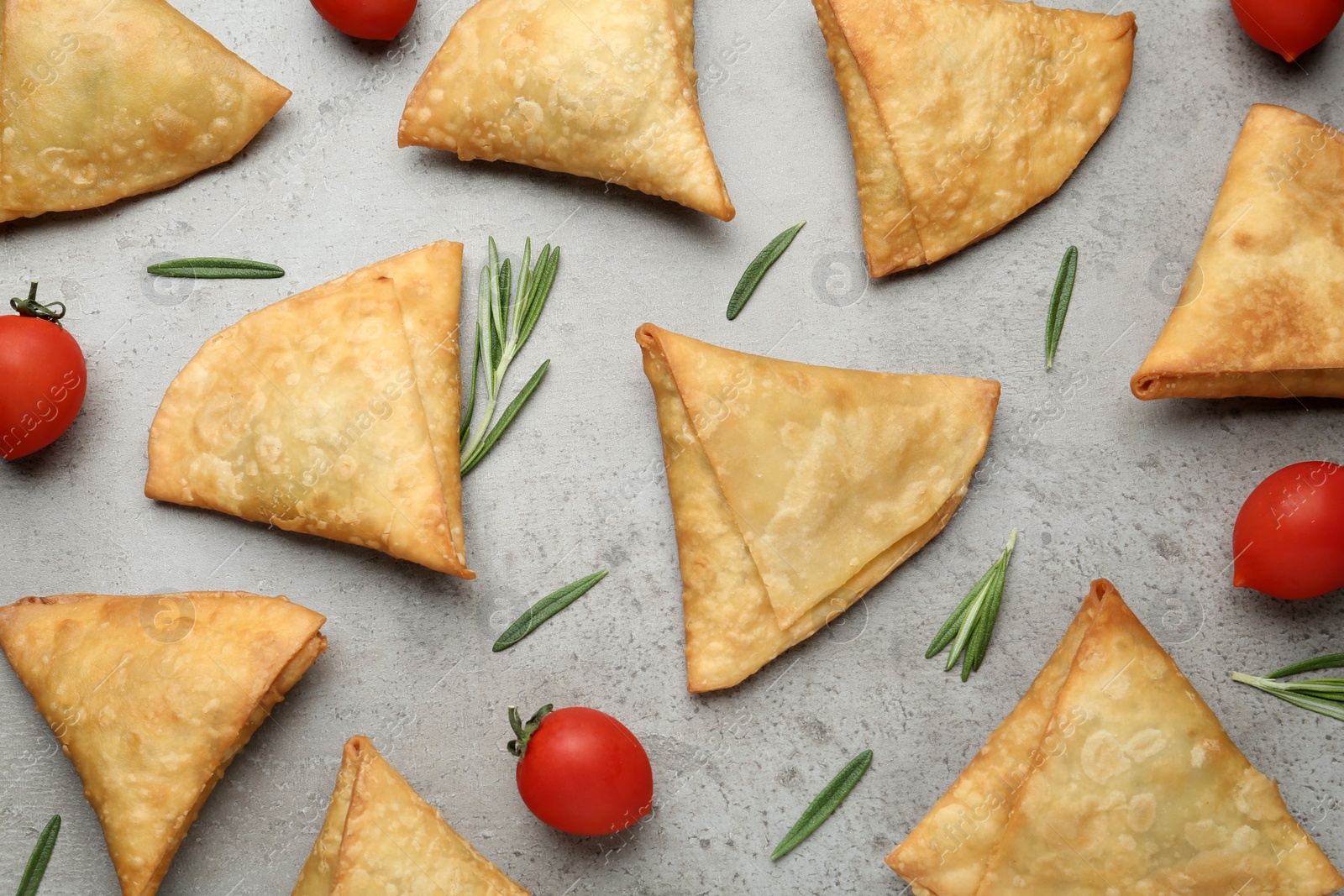 Photo of Fresh delicious crispy samosas with rosemary and tomatoes on grey table, flat lay