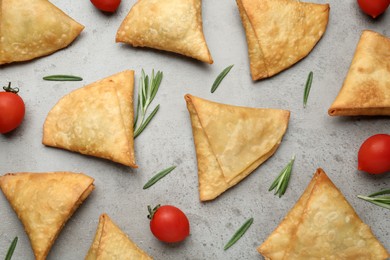 Fresh delicious crispy samosas with rosemary and tomatoes on grey table, flat lay