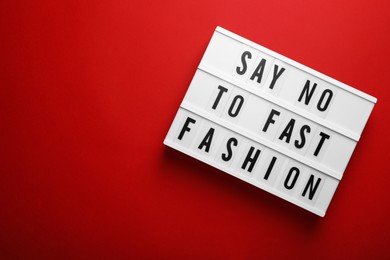 Photo of Lightbox with phrase SAY NO TO FAST FASHION on red background, top view. Space for text