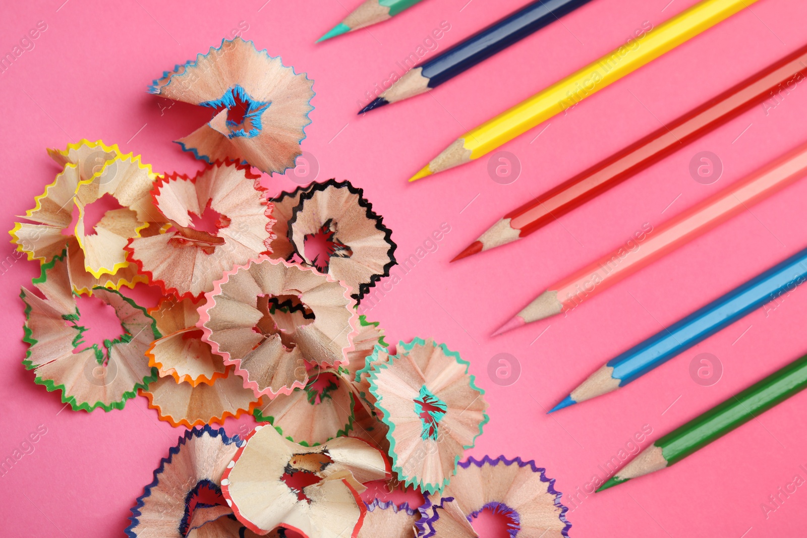 Photo of Color pencils and shavings on pink background, flat lay