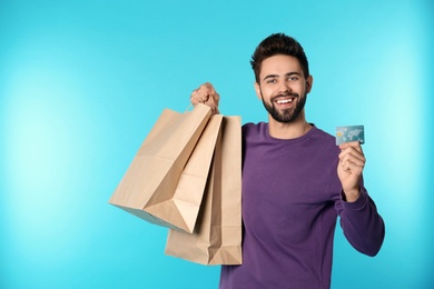 Portrait of happy young man with credit card and shopping bags on color background, space for text. Spending money
