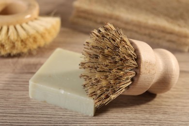 Photo of Cleaning brush and soap bar on wooden table, closeup