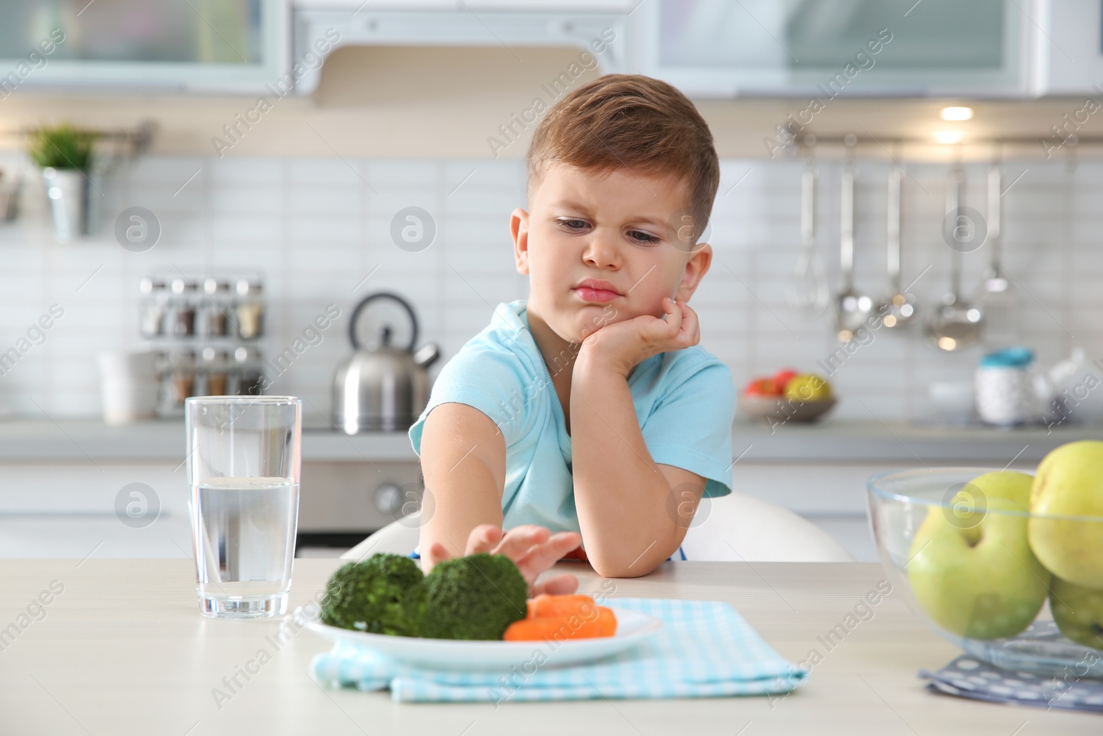 Photo of Adorable little boy refusing to eat vegetables at table in kitchen