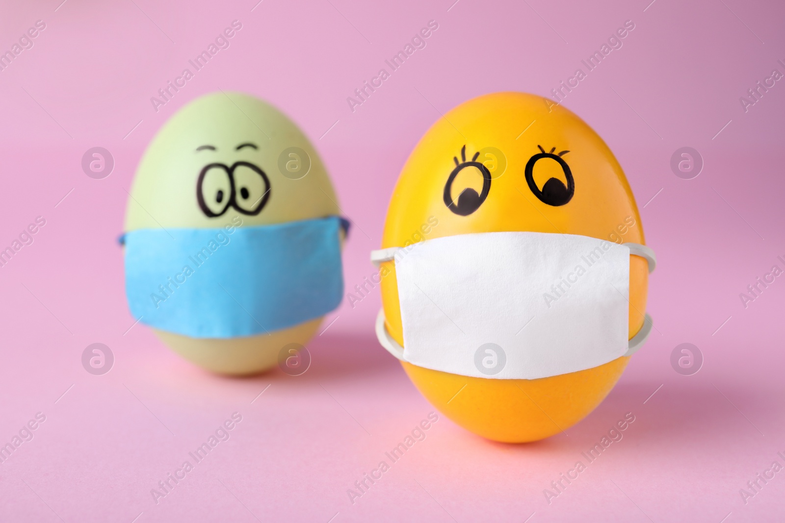 Photo of Bright eggs in protective masks on pink background. Easter holiday during coronavirus quarantine