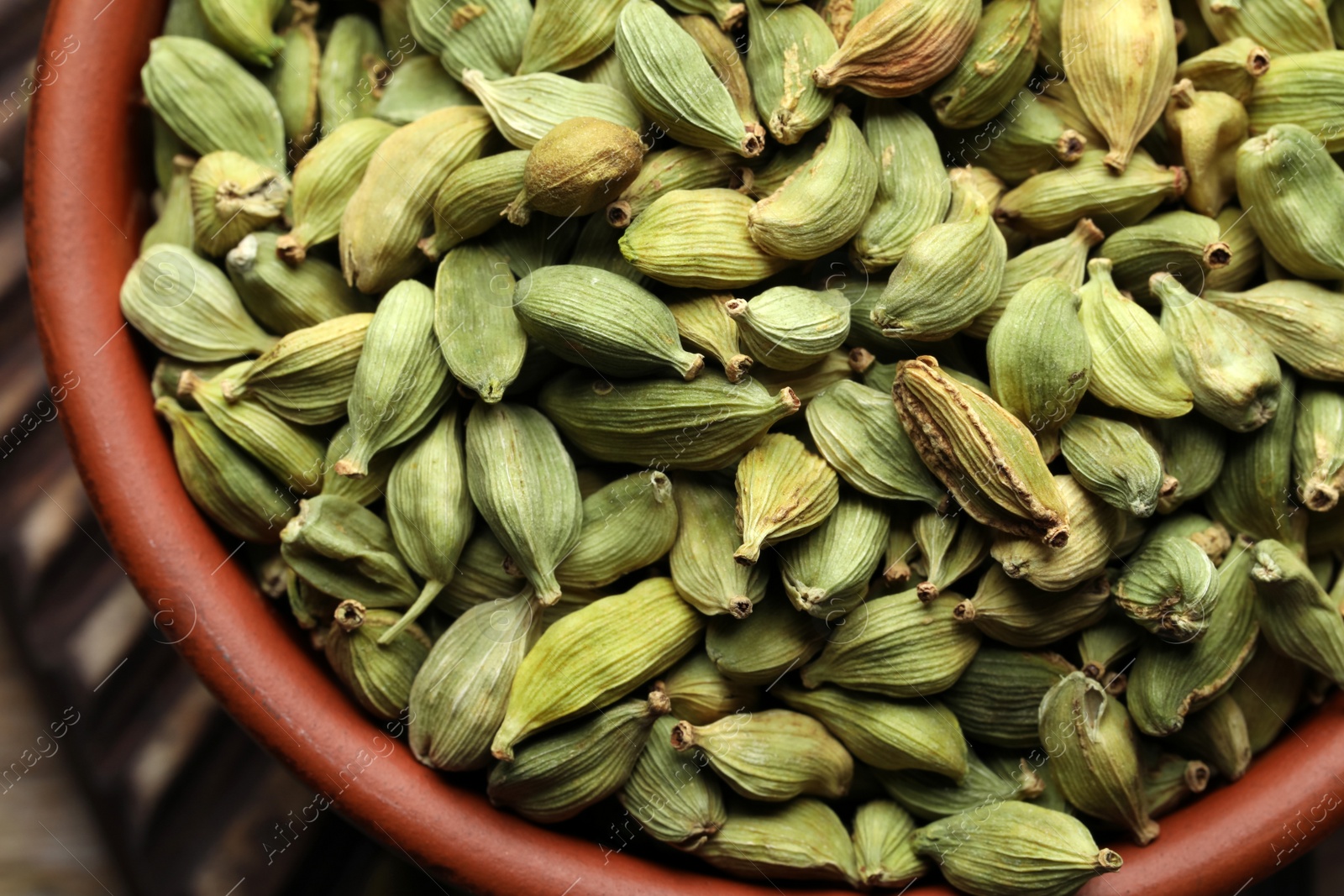 Photo of Bowl of dry cardamom pods on wooden table, closeup