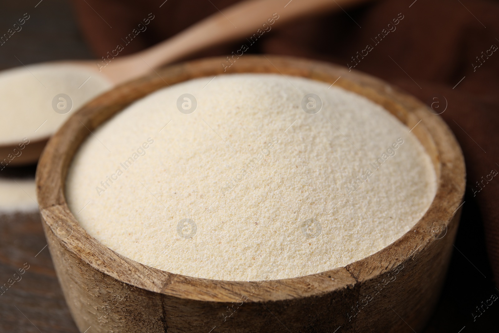 Photo of Uncooked organic semolina in bowl and spoon on wooden table, closeup