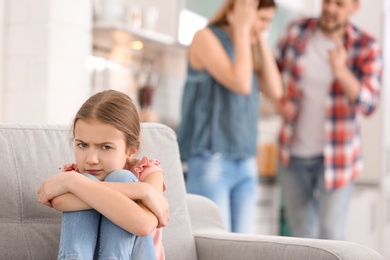 Photo of Little unhappy girl sitting on sofa while parents arguing at home