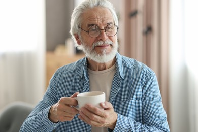 Portrait of happy grandpa with glasses and cup of drink indoors