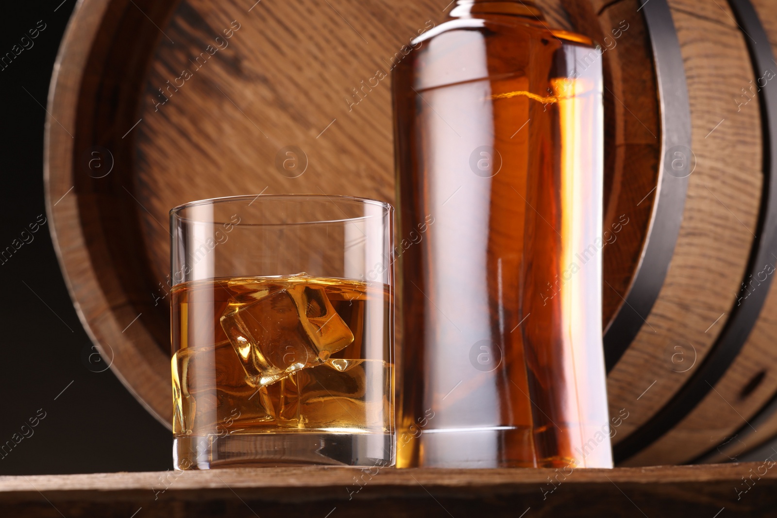 Photo of Whiskey with ice cubes in glass, bottle and barrel on wooden table