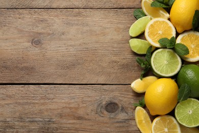 Fresh ripe lemons, limes and mint leaves on wooden background, flat lay. Space for text