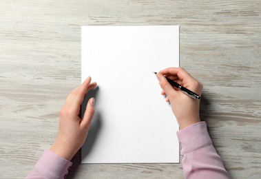 Photo of Woman writing on sheet of paper with pen at wooden table, top view