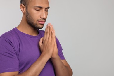 Photo of African American man with clasped hands praying to God on light grey background. Space for text