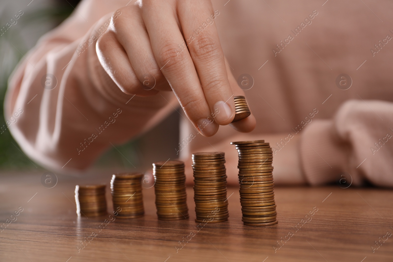 Photo of Woman stacking coins at wooden table indoors, closeup