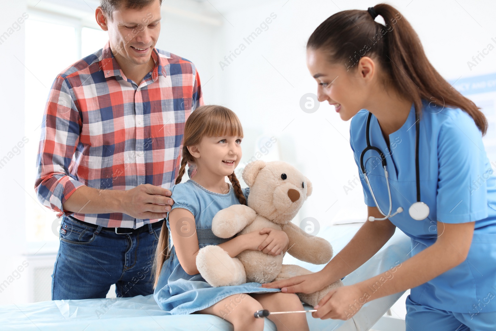 Photo of Children's doctor examining little girl near parent in hospital