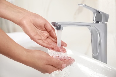 Photo of Young woman washing hands over sink in bathroom, closeup