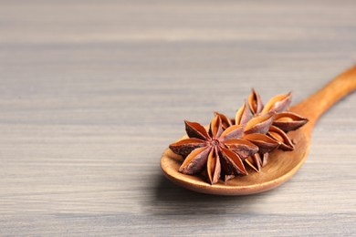 Photo of Spoon with aromatic anise stars on wooden table, space for text