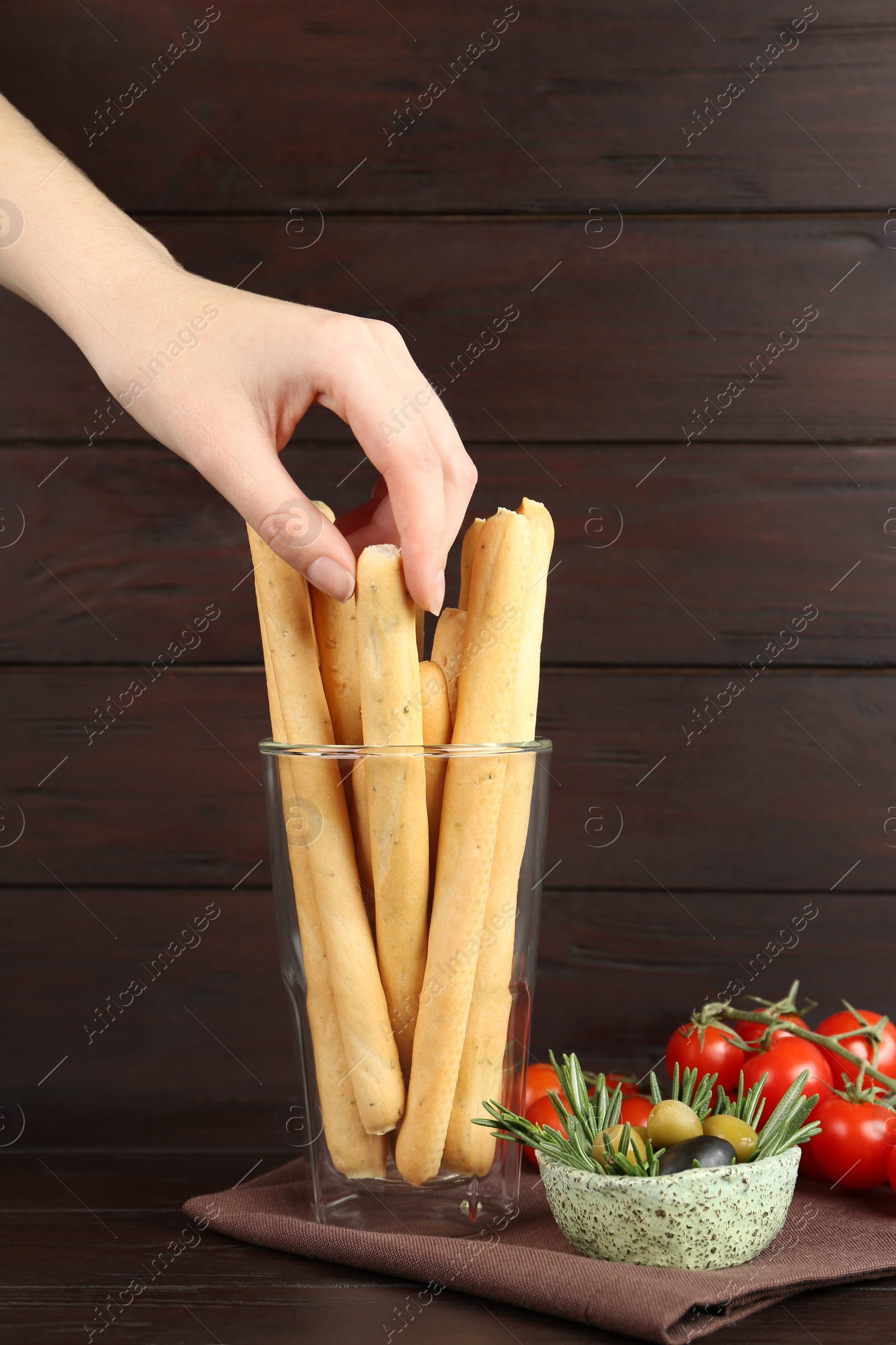Photo of Woman taking fresh delicious grissino from glass at wooden table, closeup